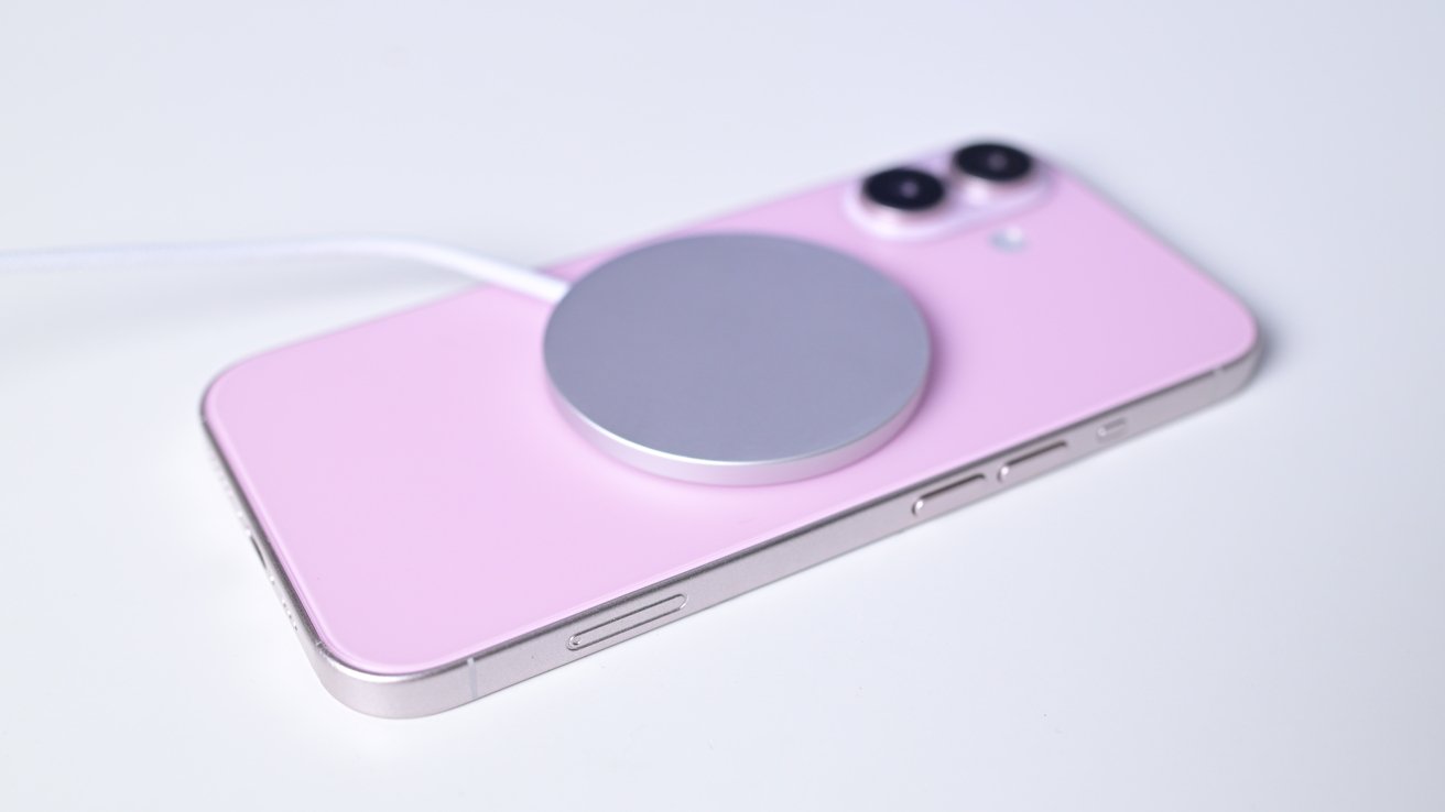 A pink iPhone 16 dummy with the new MagSafe charger on the back while sitting on a white table