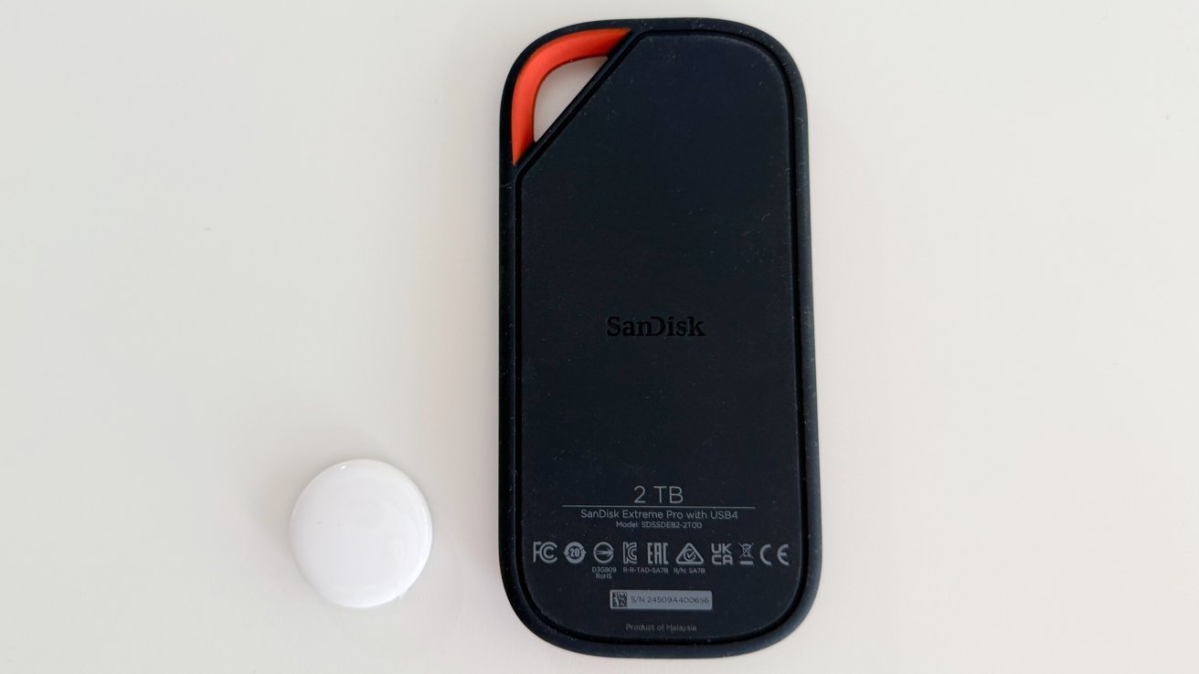 Black SanDisk external hard drive with orange accent and white circular object on a light surface.